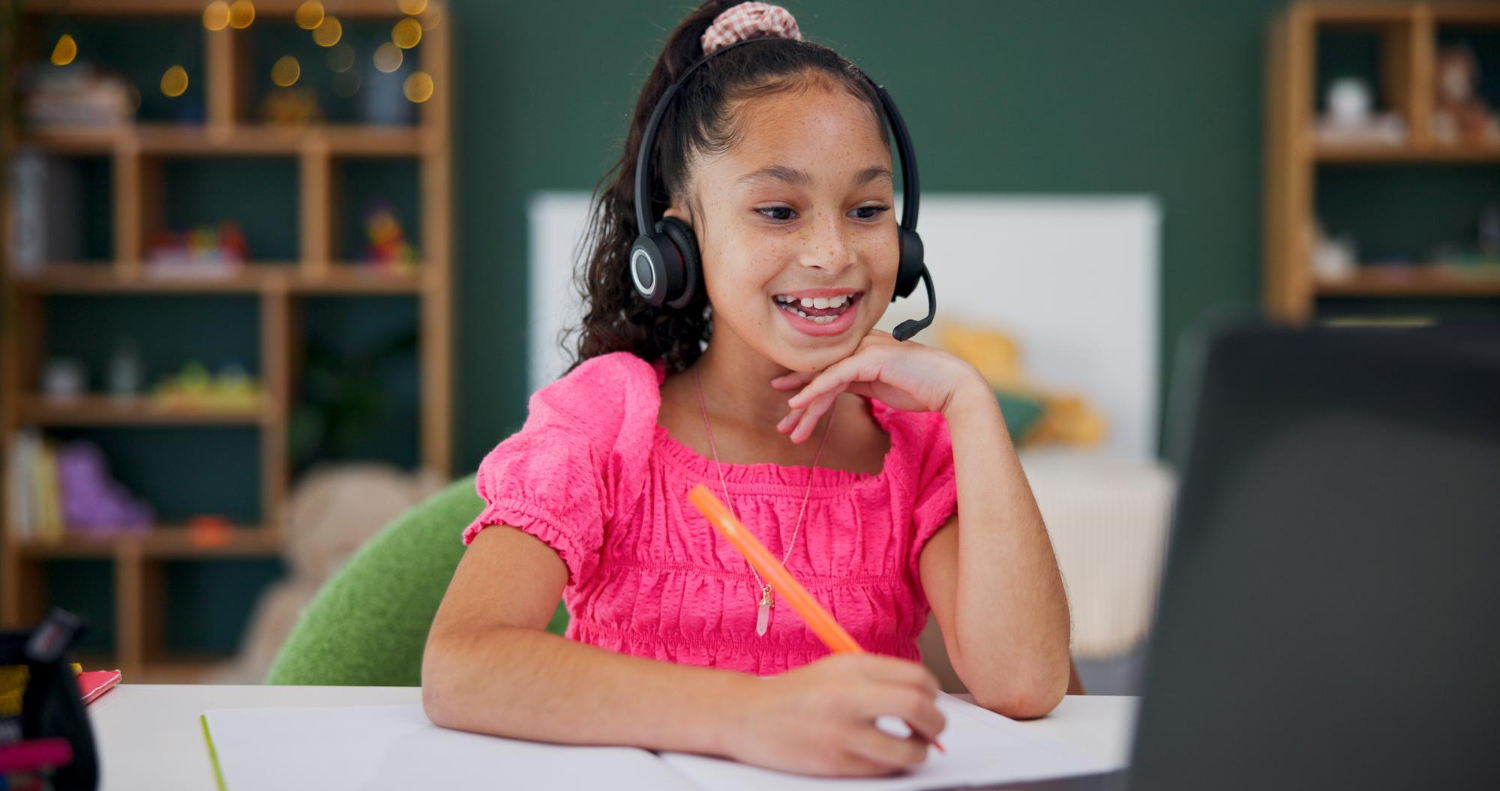 Online elementary school student learning from Wellspring Young girl with headphones smiling during online elementary school class